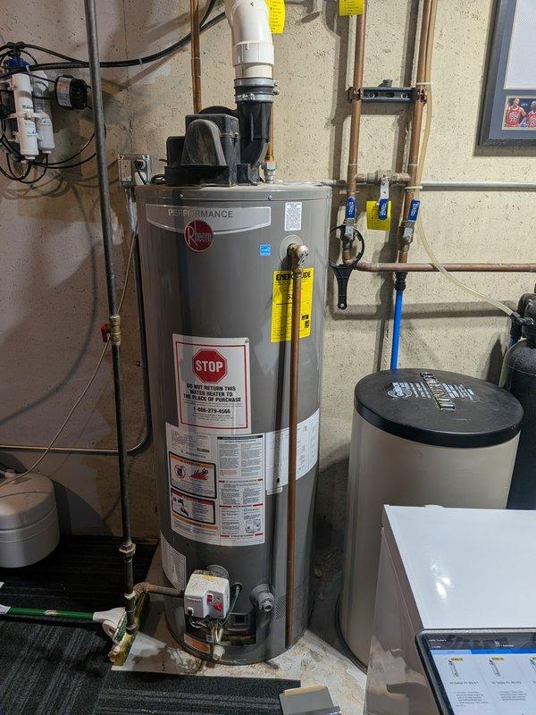 Responded to water heater leak complaint on 8-year-old Rheem unit. Upon inspection, found active leaking from bottom of tank with drip pan overflowing onto floor. Confirmed tank failure due to internal corrosion typical of unit age. Documented conditions with photos showing water accumulation in drip pan and surrounding plumbing connections. Advised customer that water heater tank has reached end of service life and requires replacement, as leaking tanks cannot be repaired.
