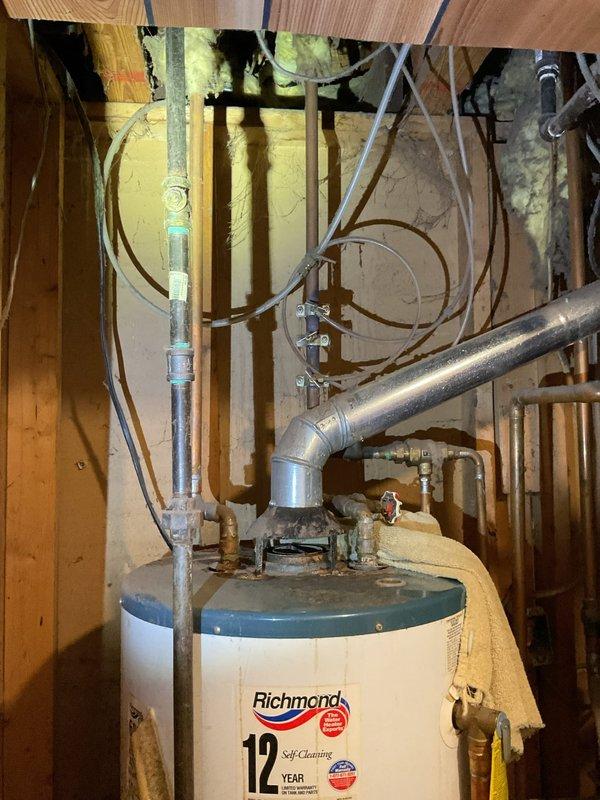 Responded to service call for leaking water heater in residential basement. Upon arrival, contacted customer prior to entry due to multiple pets on premises. Customer had limited mobility, so proceeded directly to basement utility area for assessment. Inspected 10+ year old Richmond brand 12-year self-cleaning water heater and identified active leak condition. Given the age of the unit and leak severity, recommended replacement. Documented existing installation with photographs showing plumbing connections, venting configuration, and surrounding utility infrastructure including copper supply lines, galvanized vent piping, pressure relief valve, and electrical conduit. Unit showed signs of age-related deterioration consistent with expected lifespan. Provided customer with replacement options and recommendations for new water heater installation.