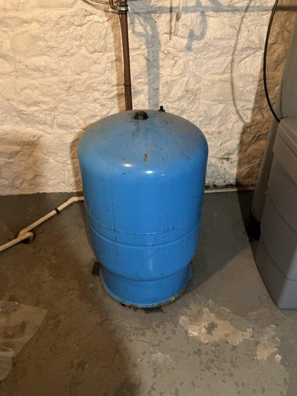 Responded to service call for water leak from pressure tank resulting in loss of water supply. Upon inspection, found 20-year-old blue pressure tank with visible signs of age, corrosion, and deterioration including rust spots on upper portion and worn paint around seams and base. Tank exhibited active leak requiring immediate attention. Documented existing conditions with photos showing corroded tank, copper piping connections, and water damage evidence on concrete floor. Completed work order and provided client with assessment of aging pressure tank system.