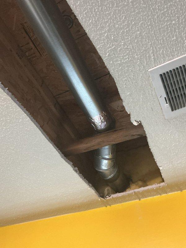 Completed installation of HVAC access line by cutting ceiling opening and routing ductwork through attic space. Created proper access point with framed opening in textured drywall ceiling, installed metallic duct with elbow fitting, and coordinated flexible ductwork connections in attic cavity alongside existing yellow supply line and wooden support structures.