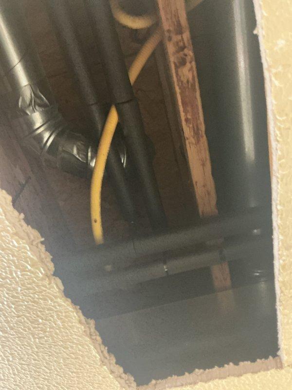 Completed installation of HVAC access line by cutting ceiling opening and routing ductwork through attic space. Created proper access point with framed opening in textured drywall ceiling, installed metallic duct with elbow fitting, and coordinated flexible ductwork connections in attic cavity alongside existing yellow supply line and wooden support structures.