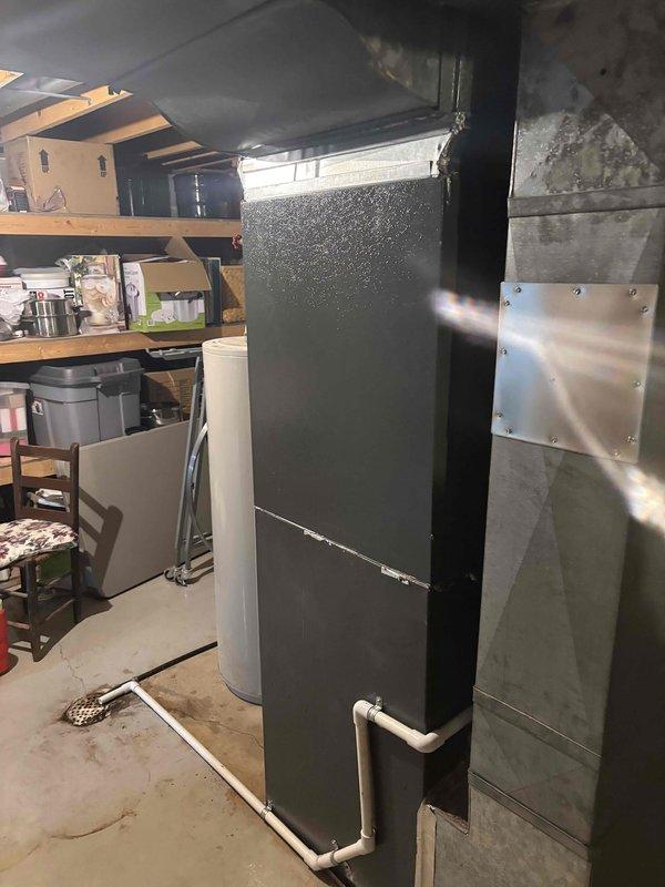 Completed full air conditioning system replacement in residential basement utility area. Removed existing AC unit and installed new air handler with proper drainage connections using white PVC piping routed along concrete floor. Secured unit adjacent to existing structural support column and integrated with existing ductwork system. Verified proper condensate management, tested all electrical connections, and confirmed system operation. Unit installed with appropriate clearances for future service access while maintaining storage functionality in surrounding area.