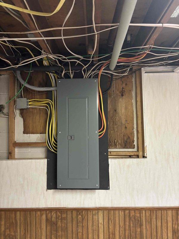 Completed 200-amp electrical service upgrade at residential property. Coordinated utility company power disconnect and reconnect to facilitate safe installation of new main service panel. Customer prepared work area by removing ceiling tiles and built box enclosure surrounding existing panel to provide full access. Installed new gray electrical breaker panel with proper wire management, routing multiple branch circuits including yellow, orange, white, and additional colored cables in organized configuration through ceiling joists. Installed exterior electrical meter box with vertical conduit run along siding and weatherhead mast assembly on roof for utility connection. Obtained electrical permit and scheduled final inspection. All work completed to code specifications with power successfully restored following utility reconnect.