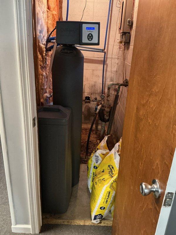 Performed on-site evaluation for water softener replacement estimate at residential property. Inspected existing Culligan water conditioning system currently installed in utility closet with adequate plumbing infrastructure including copper supply lines, brass fittings, and PVC drain configuration. System operational with digital control panel functioning properly and salt supply present. Assessed installation location featuring white tile walls, concrete flooring, and sufficient clearance for equipment access and maintenance. Documented existing plumbing layout including vertical and horizontal blue PVC piping network, connection points on concrete block wall, and proximity to water heater. Photographed current system configuration, utility room conditions, and available workspace for potential replacement installation. Reviewed customer interest in alternative water conditioning solutions and service options compared to current provider.