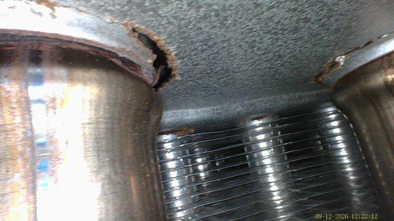 Performed inspection on 16-year-old furnace to assess operational condition and determine if unit is safe to continue using. Documented existing ductwork showing signs of rust, corrosion, and deterioration at connection points, particularly visible on cylindrical duct sections and flexible connector transitions. Photographed HVAC system components including duct penetrations through ceiling, evaporator coil assembly, and insulated ductwork in confined mechanical space to provide visual record of current equipment condition for customer decision-making regarding repair versus replacement options.