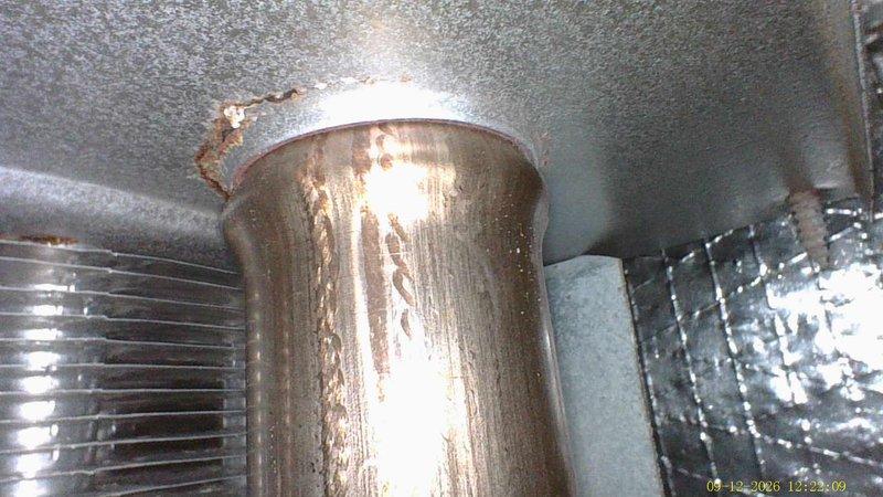 Performed inspection on 16-year-old furnace to assess operational condition and determine if unit is safe to continue using. Documented existing ductwork showing signs of rust, corrosion, and deterioration at connection points, particularly visible on cylindrical duct sections and flexible connector transitions. Photographed HVAC system components including duct penetrations through ceiling, evaporator coil assembly, and insulated ductwork in confined mechanical space to provide visual record of current equipment condition for customer decision-making regarding repair versus replacement options.