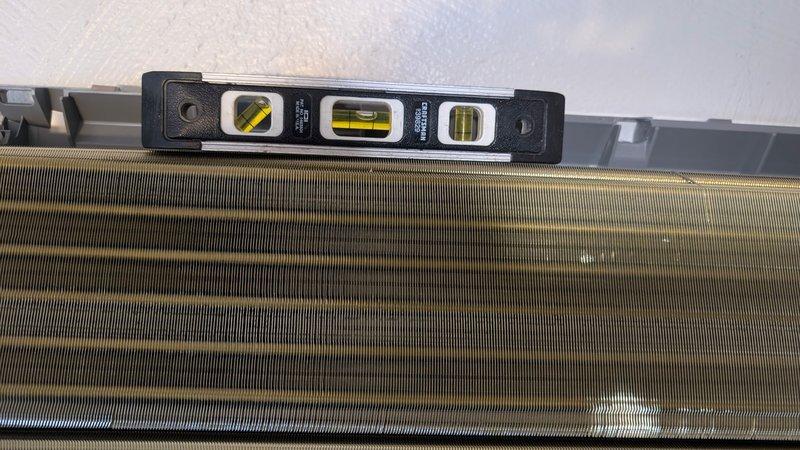 Responded to service call for newly installed mini split system experiencing water leakage. Upon arrival, discovered indoor unit was not properly leveled, causing condensate drainage issues. Used torpedo level to verify improper pitch on both the air handler and evaporator coil assembly. Adjusted mounting bracket and repositioned unit to achieve correct horizontal alignment, ensuring proper condensate flow to drain line. Verified level positioning across filter compartment and finned coil section. Tested system operation and confirmed water now draining properly without leakage.