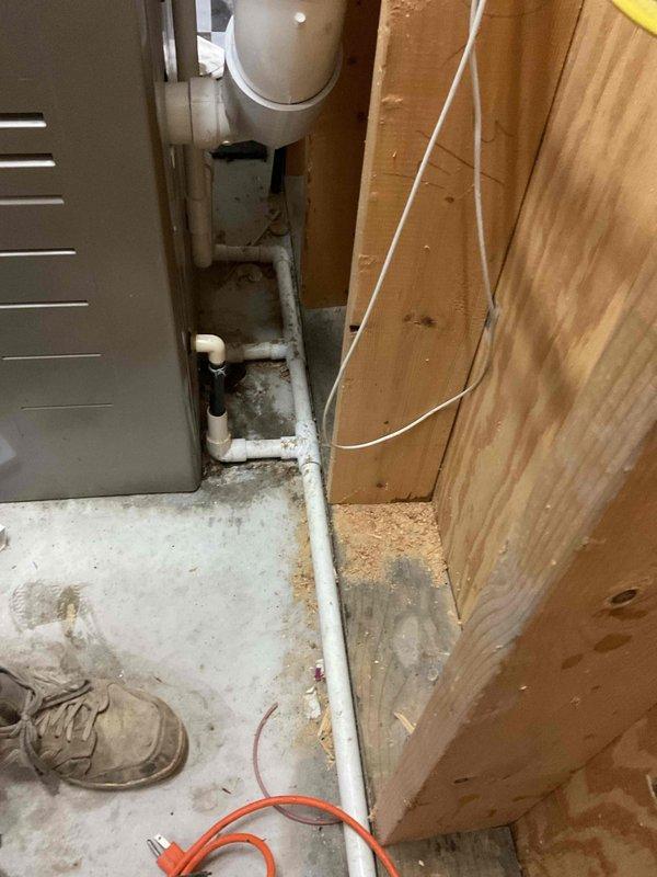 # IAQ-MISC Service Completed

Responded to report of leak in basement utility area. Upon arrival, conducted visual inspection of exposed plumbing system and HVAC components. Identified active moisture intrusion evidenced by water staining and dark patches on concrete floor near PVC drain pipe connections. Photographed affected areas showing white PVC plumbing assembly, adjacent air handler unit, and compromised floor surfaces with visible efflorescence and mineral deposits indicating ongoing water exposure. Documented condition of pipe fittings and connections at base of vertical drain line where moisture accumulation was most prevalent.