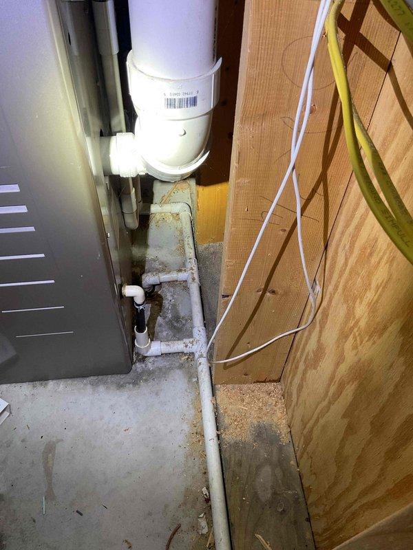# IAQ-MISC Service Completed

Responded to report of leak in basement utility area. Upon arrival, conducted visual inspection of exposed plumbing system and HVAC components. Identified active moisture intrusion evidenced by water staining and dark patches on concrete floor near PVC drain pipe connections. Photographed affected areas showing white PVC plumbing assembly, adjacent air handler unit, and compromised floor surfaces with visible efflorescence and mineral deposits indicating ongoing water exposure. Documented condition of pipe fittings and connections at base of vertical drain line where moisture accumulation was most prevalent.