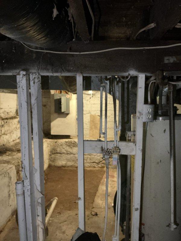 Provided estimate for replacement of 35-year-old standard tank water heater originally manufactured in 1991. Unit has reached end of expected service life and requires full replacement. Documented existing installation conditions in unfinished basement area with photographic records showing structural support elements, mechanical systems layout, and current equipment placement for accurate replacement planning.