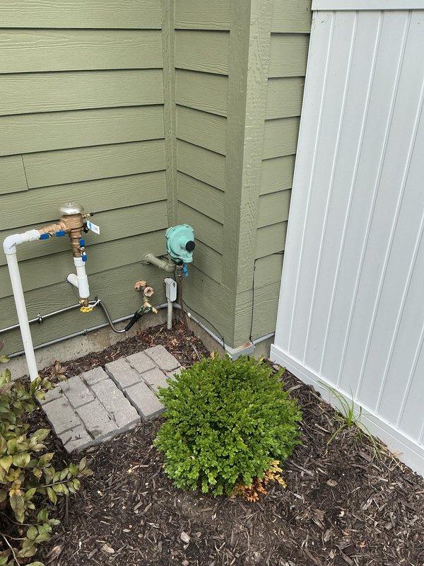 Completed on-site assessment for conversion of residential standby generator from liquid propane to natural gas fuel source. Evaluated existing generator installation, including current LP gas supply line configuration, electrical disconnect panel, and conduit routing along exterior wall. Inspected gas meter location and existing utility connections to determine feasibility of natural gas conversion.

Assessed required gas line routing from meter to generator location at rear of residence. Measured distance and documented obstacles including landscaping, mulched areas, and structural components. Identified optimal path for new gas line installation to minimize disruption to existing hardscape and plantings. Documented current plumbing infrastructure at building corner, including PVC piping, brass fittings, and existing valve assemblies to ensure proper clearances for new gas line routing.

Photographed all relevant equipment and utility connections for conversion estimate preparation. 