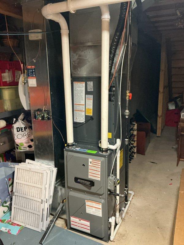 Completed full HVAC system replacement including outdoor condensing unit and indoor air handler/furnace. Removed existing equipment and installed new gray cabinet furnace unit in basement utility area with proper PVC intake and exhaust venting configuration. Mounted new outdoor heat pump/AC unit on concrete pad with proper clearances from building structure. Installed gray electrical disconnect box on exterior wall with code-compliant conduit routing to outdoor unit. Connected refrigerant lines between indoor and outdoor components using copper lineset. Verified all electrical connections, tested system operation, and confirmed proper airflow through ductwork connections.