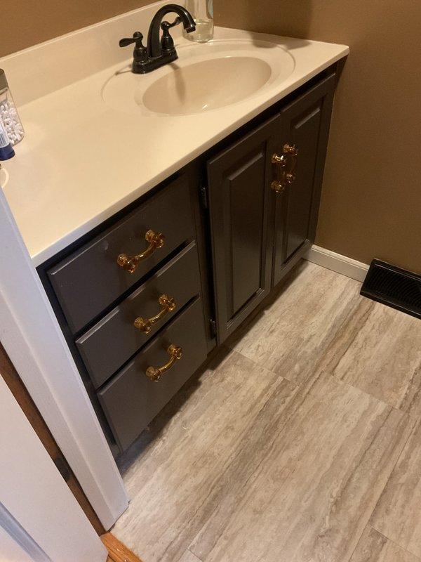 Completed return visit to assess and provide estimates for two additional bathroom vanity replacements. Documented existing vanity configurations including a dark gray raised-panel cabinet with integrated white countertop sink, bronze fixtures, and hardware details. Measured clearances and specifications for both vanity locations to prepare accurate replacement quotes.