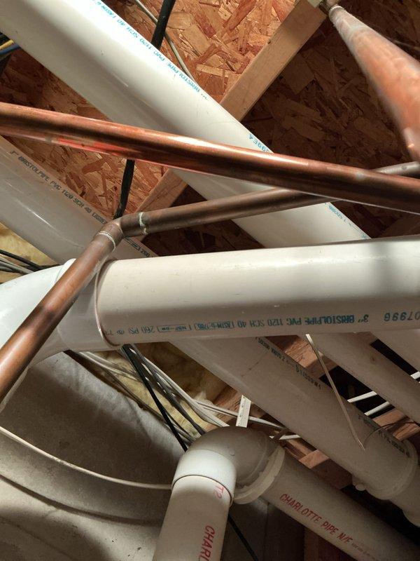 Responded to no hot water call and found 6-year-old standard tank water heater leaking from top ring with water running down the side of unit. Leak was contained in drain pan with no water damage to basement floor. Documented equipment condition with photos showing water heater installation, plumbing connections, and overhead piping configuration including PVC discharge lines and copper supply lines.