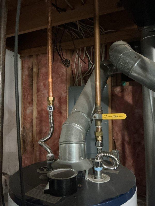 Responded to service call for leaking water heater in residential basement utility area. Upon arrival, inspected 10-year-old water heater unit and surrounding plumbing connections, including copper supply lines, flexible connectors, and associated brass fittings. Documented existing installation configuration with water heater positioned against unfinished wall framing with exposed insulation. Photographed unit showing dark blue tank body with gray metal top section, multiple pipe connections, PVC/metal ductwork, flexible metallic gas connector, and safety valve components. Assessed leak source and overall system condition to provide customer with repair or replacement recommendations.