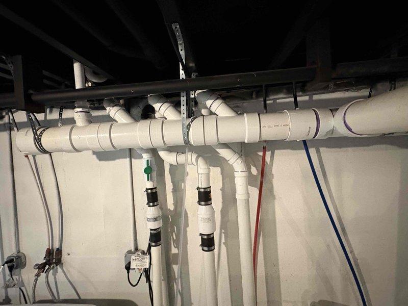 Completed installation of new sump pump system in basement utility area. Installed pump unit in basin with proper discharge piping configuration using white PVC pipe with appropriate fittings, joints, and support strapping secured to ceiling joists. All connections were properly cemented and tested for secure operation and drainage flow.