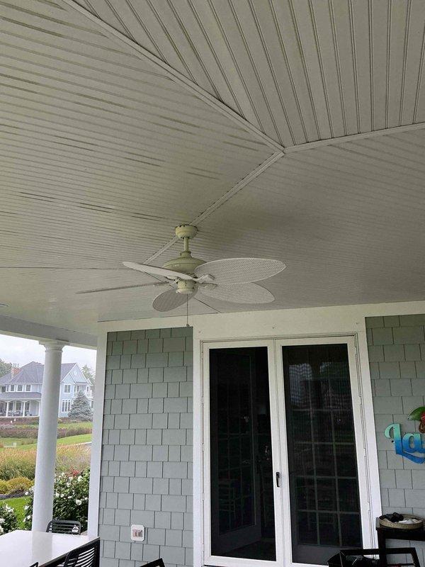 Responded to service call for non-functioning outdoor ceiling fan located on covered patio area with beadboard ceiling and green shingle siding. Removed existing failed ceiling fan unit from mounting bracket. Installed new outdoor-rated replacement ceiling fan with woven wicker-style blades and sage-colored motor housing, securing to existing electrical box and downrod. Verified proper electrical connections, tested fan operation at all speeds, and confirmed pull chain functionality. Customer was not present during service visit; accessed property using provided gate and garage codes.