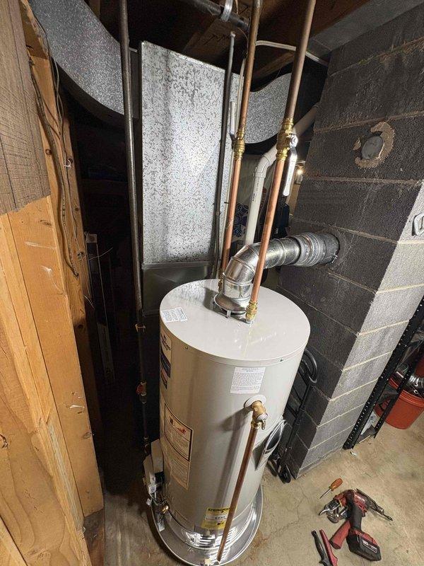 Completed installation of 40-gallon natural gas water heater with 6-inch vent and short configuration in basement utility area. Unit was positioned against cinder block wall with proper copper supply line connections, brass fittings, and metallic venting installed to manufacturer specifications. All plumbing connections were secured and tested for proper operation.