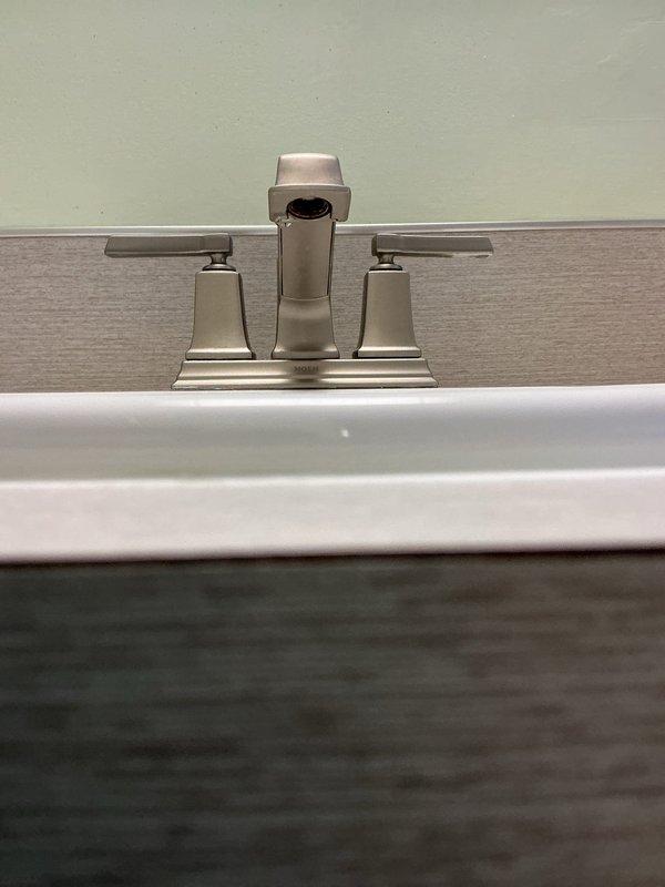 Replaced bathroom faucet with new two-handle brushed nickel fixture featuring lever handles and central spout mounted on rectangular base plate. Verified proper installation of braided stainless steel supply lines connected to shut-off valves and confirmed P-trap drain assembly functioning correctly with no leaks detected.