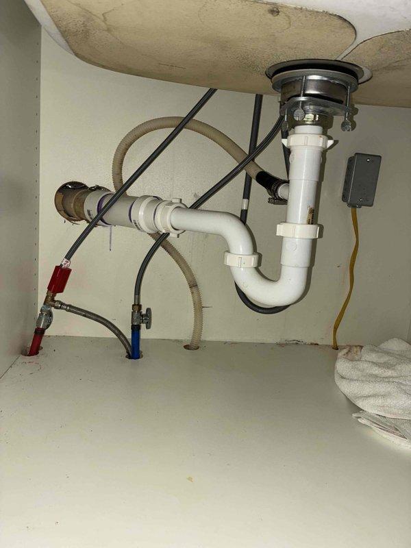 Responded to kitchen water leak complaint with water found under sink and on floor following overnight dishwasher operation. Inspected under-sink plumbing including P-trap assembly, supply lines, and drain connections. Examined cabinet interior for source of leak and documented water damage on cabinet surfaces. Verified hot and cold water supply line connections with shutoff valves and checked all flexible hose connections. Photographed plumbing configuration and affected areas for documentation purposes.