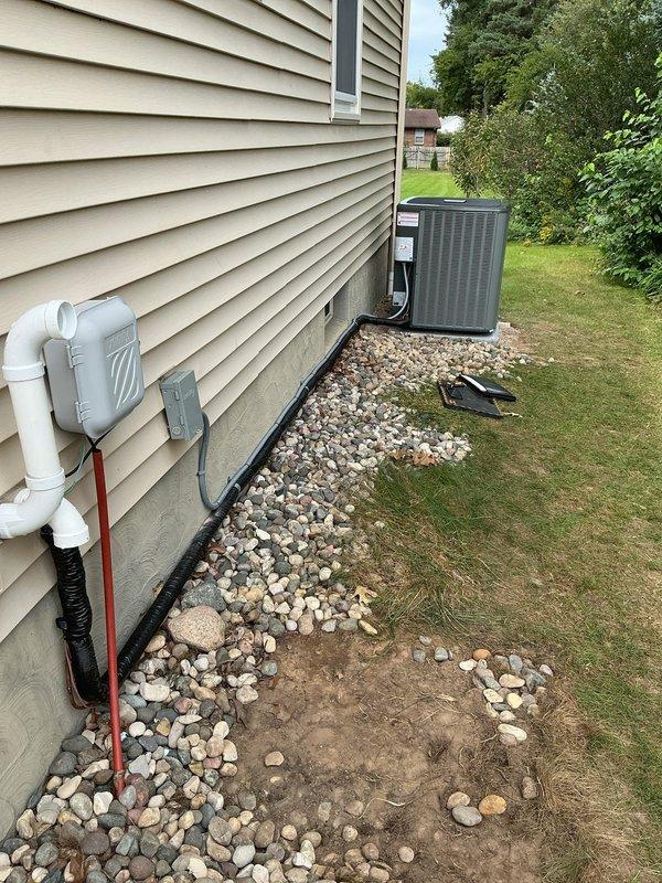 Relocated residential air conditioning condensing unit to new position along exterior foundation wall. Installed unit on concrete pad with proper clearances, ran new electrical conduit from house to unit location, and secured all connections. Verified system operation and proper drainage through existing PVC discharge line system.