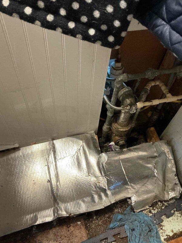 Responded to overflowing kitchen sink issue in residential kitchen. Upon inspection, found double-basin stainless steel sink with drainage concerns and mineral deposit buildup around drain assembly. Accessed plumbing system beneath sink through crawlspace access point, where aging pipes and connections showed signs of deterioration. Cleared blockage, restored proper drainage function, and documented pre-existing conditions including water staining and worn plumbing components with metallic tape repairs.