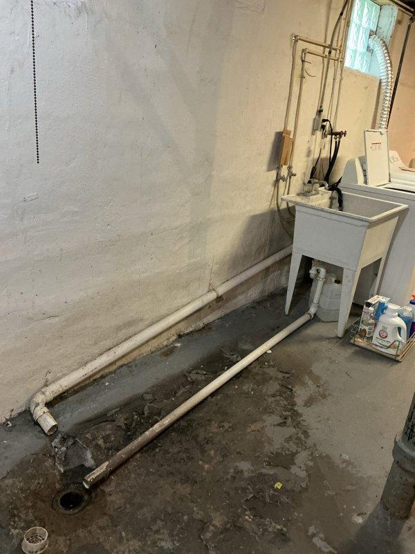 Responded to emergency water leak call with homeowner reporting unknown water source flooding basement and triggering water alarm. Upon arrival, conducted thorough inspection of basement utility area and identified active leak from deteriorated pipe connection near floor drain. Water accumulation was evident across concrete floor with significant moisture staining and pooling around exposed plumbing runs.

Traced water source to failed joint connection on older drainage pipe running across basement floor toward main drain opening. The compromised pipe section showed signs of age-related deterioration and material breakdown. Isolated the affected line and performed emergency leak repair by replacing the damaged pipe section and securing all connections with appropriate fittings. Tested system under pressure to verify repair integrity and confirm no additional leak points.

Inspected surrounding plumbing infrastructure including copper supply lines, PVC drainage system, and utility sink 