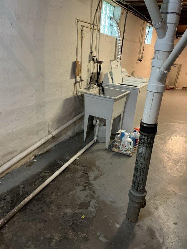 Responded to emergency water leak call with homeowner reporting unknown water source flooding basement and triggering water alarm. Upon arrival, conducted thorough inspection of basement utility area and identified active leak from deteriorated pipe connection near floor drain. Water accumulation was evident across concrete floor with significant moisture staining and pooling around exposed plumbing runs.

Traced water source to failed joint connection on older drainage pipe running across basement floor toward main drain opening. The compromised pipe section showed signs of age-related deterioration and material breakdown. Isolated the affected line and performed emergency leak repair by replacing the damaged pipe section and securing all connections with appropriate fittings. Tested system under pressure to verify repair integrity and confirm no additional leak points.

Inspected surrounding plumbing infrastructure including copper supply lines, PVC drainage system, and utility sink 