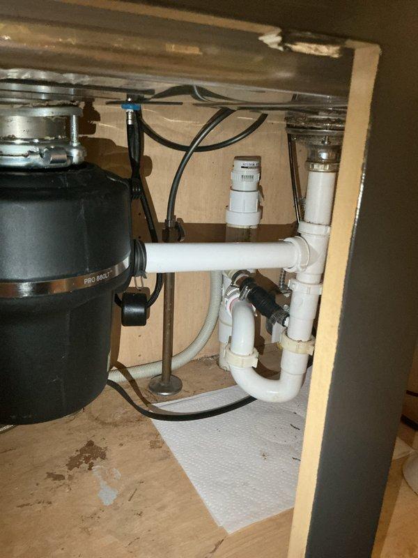 Responded to kitchen sink leak complaint. Upon inspection, identified leak originating from compromised connections in the PVC drain assembly beneath double-basin sink. The drainage system included a garbage disposal unit connected to white PVC P-trap configuration with multiple joints and elbow fittings. Inspected all visible plumbing components including disposal unit, drain connections, supply lines, and trap assembly. Tightened loose slip-joint connections at P-trap and verified proper sealing of disposal discharge connection to drain system. Tested all connections under running water to confirm leak was eliminated. Left area clean and dry with no active water discharge detected at completion.