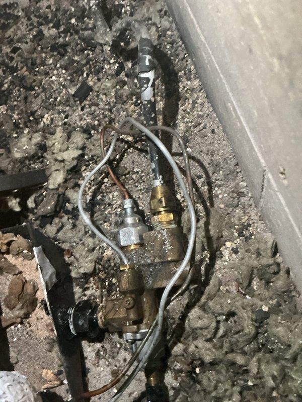 Responded to reported hissing sound from gas fireplace area in 1980s-era condo unit. Upon inspection, identified active gas leak at pilot assembly of original fireplace installation. Leak was isolated to brass fitting connection on pilot assembly mechanism. Heavy dust and debris accumulation noted throughout equipment compartment, consistent with 40+ years of service without maintenance. Documented leak location with photographic evidence showing compromised pilot assembly components. Advised on necessary repairs to pilot assembly to eliminate gas leak hazard and restore safe fireplace operation.