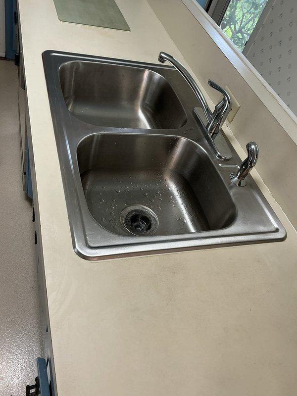 Responded to service call regarding adhesive residue from previous sink installation. Upon inspection, identified excess plumber's putty and silicone sealant deposits on countertop surface around double-basin stainless steel kitchen sink that were attracting dirt and creating sticky areas. Carefully removed all improper adhesive spots and residue using appropriate solvents and scrapers without damaging countertop or sink finish. Cleaned and degreased affected areas thoroughly. Verified proper seal integrity around sink perimeter remained intact. Left work area clean with all adhesive contamination removed and surfaces restored to proper condition.