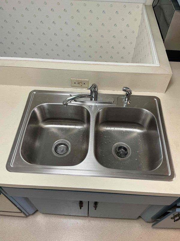 Responded to service call regarding adhesive residue from previous sink installation. Upon inspection, identified excess plumber's putty and silicone sealant deposits on countertop surface around double-basin stainless steel kitchen sink that were attracting dirt and creating sticky areas. Carefully removed all improper adhesive spots and residue using appropriate solvents and scrapers without damaging countertop or sink finish. Cleaned and degreased affected areas thoroughly. Verified proper seal integrity around sink perimeter remained intact. Left work area clean with all adhesive contamination removed and surfaces restored to proper condition.
