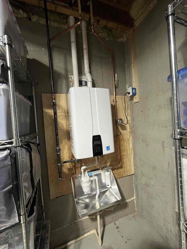 Completed installation of Energy Star certified tankless water heater in basement utility area. Unit was mounted on plywood backing secured to concrete block wall with proper clearances maintained. Connected copper supply and discharge piping with appropriate shutoff valves and configured gas line connections per manufacturer specifications. Installed condensate drain pan beneath unit with dedicated condensate pump and drainage piping to handle acidic condensate byproduct. Mounted electrical disconnect box adjacent to unit and completed all electrical connections in compliance with code requirements. Tested unit operation, verified proper ignition sequence, confirmed adequate gas pressure and flow rates, and programmed temperature settings on digital control panel. System is fully operational and producing hot water on demand.