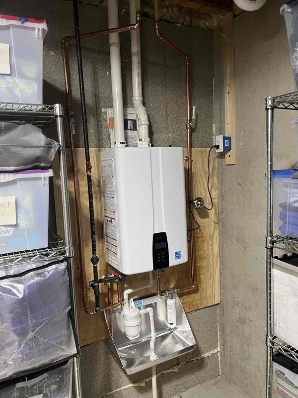 Completed installation of Energy Star certified tankless water heater in basement utility area. Unit was mounted on plywood backing secured to concrete block wall with proper clearances maintained. Connected copper supply and discharge piping with appropriate shutoff valves and configured gas line connections per manufacturer specifications. Installed condensate drain pan beneath unit with dedicated condensate pump and drainage piping to handle acidic condensate byproduct. Mounted electrical disconnect box adjacent to unit and completed all electrical connections in compliance with code requirements. Tested unit operation, verified proper ignition sequence, confirmed adequate gas pressure and flow rates, and programmed temperature settings on digital control panel. System is fully operational and producing hot water on demand.