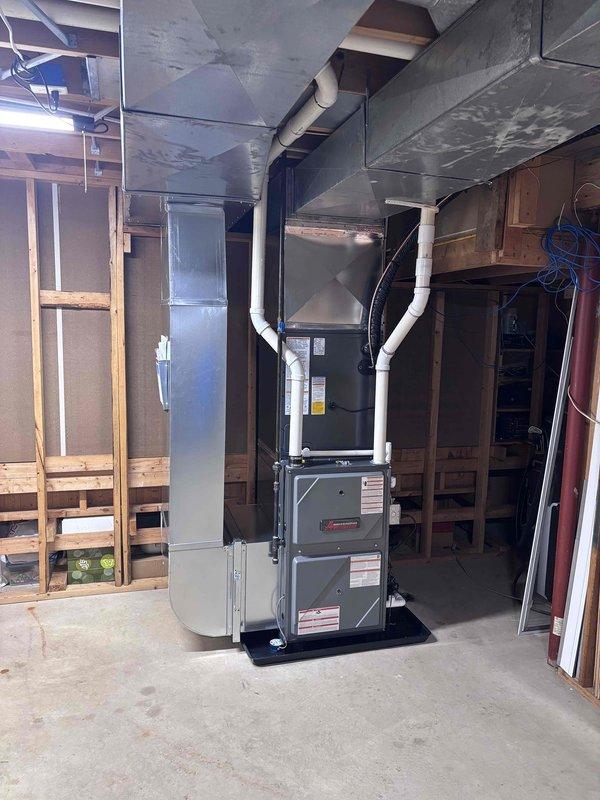 Completed full residential HVAC system installation including new furnace and air conditioning condenser unit. Installed gray metal furnace in basement with proper venting using white PVC piping, connected to new ductwork system with Y-branch configurations extending to existing trunk lines. Mounted outdoor AC condenser on concrete pad against exterior wall with beige vinyl siding, installed refrigerant line set with black insulation running from outdoor unit to indoor coil, and completed electrical connections with disconnect box mounted on exterior wall. Verified all connections, tested system operation, and confirmed proper airflow through ductwork. Installation completed per manufacturer specifications with all components operational.