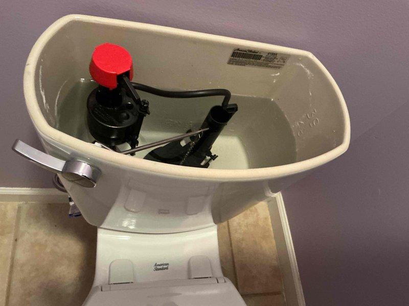 Responded to complaint of water leaking from fill valve during toilet flush cycle. Upon arrival, removed tank lid and inspected internal flush mechanism on American Standard two-piece toilet. Identified faulty fill valve assembly with red cap causing water discharge from top of valve during refill operation. Replaced defective fill valve with new unit, reconnected refill tube to overflow pipe, and adjusted water level to manufacturer specifications. Cycled flush mechanism multiple times to verify proper operation and confirm no leakage from valve assembly. Tank now refills correctly without water spraying from top of fill valve. Photographed completed repair for service records. Unit tested and returned to normal operation.