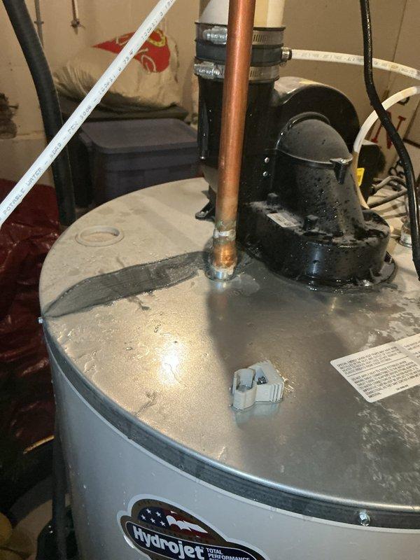 Responded to water heater leak complaint on 9-year-old Bradford White unit located in basement. Upon inspection, found water heater leaking at bottom into drain pan with visible moisture and condensation on top surface. Documented unit condition with photos showing Hydrojet-branded water heater with connected copper piping, circulation pump, and evidence of previous repair attempts with sealant/tape on top surface. Advised customer that leak at bottom of tank indicates internal tank failure, which is not repairable, and recommended full water heater replacement due to age and condition of unit.