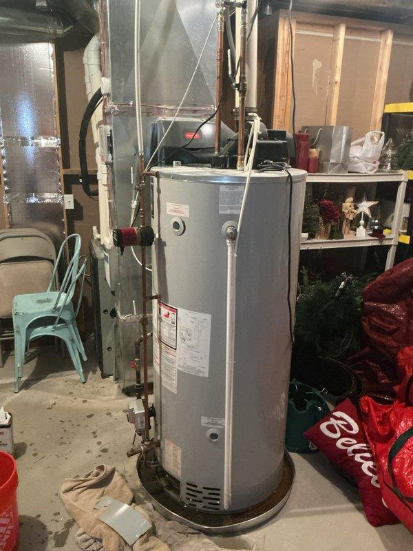 Responded to water heater leak complaint on 9-year-old Bradford White unit located in basement. Upon inspection, found water heater leaking at bottom into drain pan with visible moisture and condensation on top surface. Documented unit condition with photos showing Hydrojet-branded water heater with connected copper piping, circulation pump, and evidence of previous repair attempts with sealant/tape on top surface. Advised customer that leak at bottom of tank indicates internal tank failure, which is not repairable, and recommended full water heater replacement due to age and condition of unit.