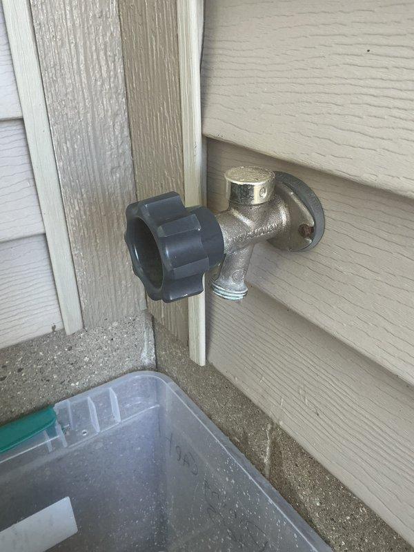 Responded to service call for leaking outdoor hose bib. Upon inspection, found standard brass spigot with wheel-style handle valve mounted on exterior wall above foundation level showing signs of weathering, corrosion, and mineral deposits. Diagnosed leak source, performed necessary repairs to stop water discharge, and tested fixture to confirm proper operation. Documented completed work with photographs showing spigot assembly, wall mounting, and surrounding installation area.