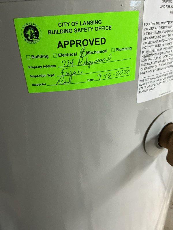 Responded to service call for water heater producing loud screeching sound with water present in drain pan. Upon inspection, found 6-year-old Bradford White water heater in basement utility area with visible water accumulation in collection tray. Identified source of screeching noise as failing temperature and pressure relief valve. Inspected all plumbing connections, copper supply lines, and drain pan for signs of active leaking or corrosion. Documented current condition of unit with photographs showing mechanical installation, City of Lansing mechanical inspection approval sticker dated 7-16-2020, and overall system configuration. Advised customer of findings and recommended immediate replacement of faulty T&P relief valve to eliminate noise and prevent potential safety hazard.