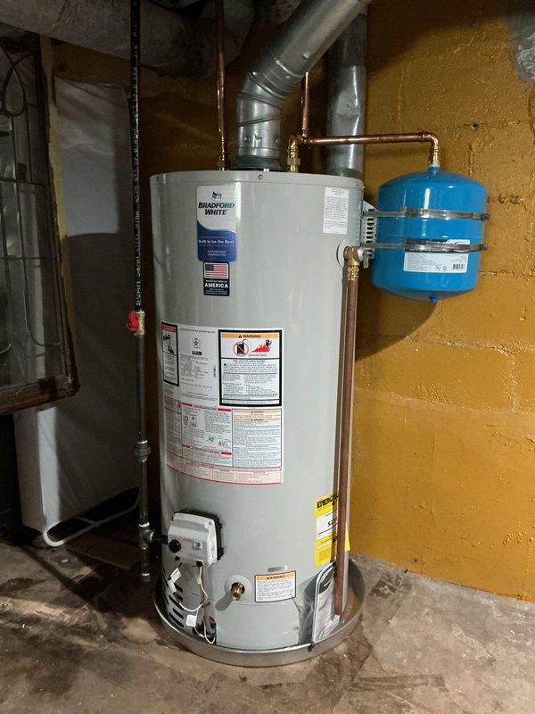 Completed installation of a 40-gallon natural gas Bradford White water heater in basement utility area. Unit was properly vented with metallic ductwork, connected to copper supply lines, and equipped with a blue expansion tank with brass fittings to protect the system from thermal expansion. All connections were secured, safety labels verified, and the installation meets code requirements for residential water heating systems.