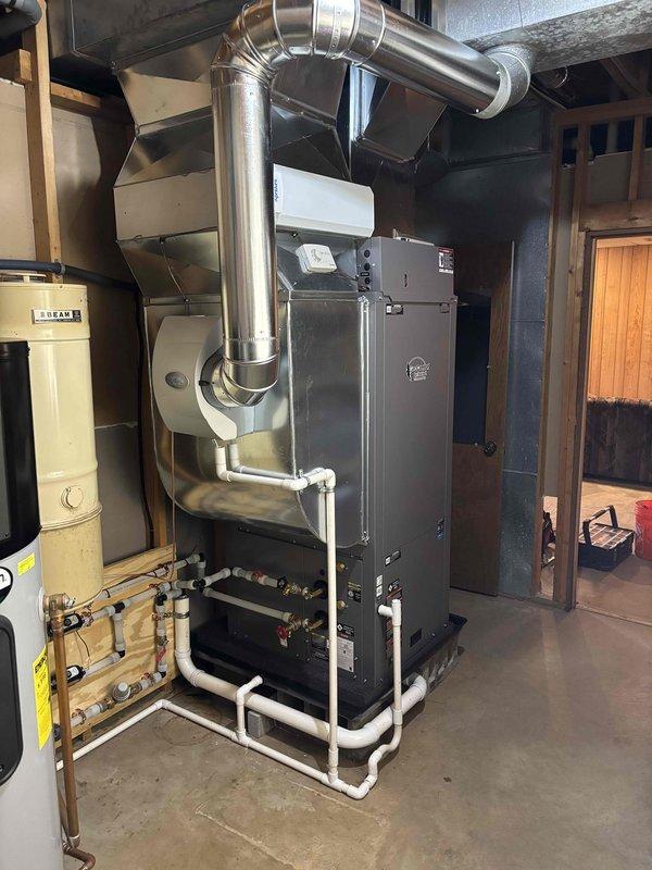 Completed full geothermal HVAC system installation in residential basement utility room. Installed and positioned geothermal heat pump unit on wooden pallet with proper elevation, connected metallic supply and return ductwork to existing distribution system, and integrated stainless steel flue piping with 90-degree transitions extending to exterior termination point. Established all necessary copper piping connections with white insulation wrapping, installed PVC condensate drain lines, and connected water heater integration with pressure relief valves and circulation components. Secured all mechanical equipment to code specifications, verified proper electrical connections to panel box, ensured all manufacturer labels and safety warnings remained visible, and conducted system pressure testing. Installation completed with all components operational and ready for commissioning.