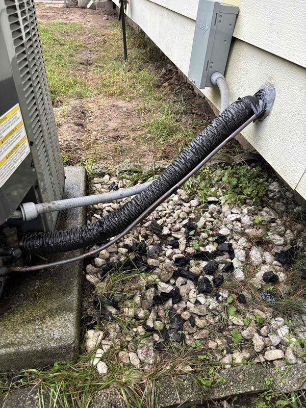 Completed annual cooling maintenance and tune-up on residential air conditioning system. Customer reported experiencing cold air from the unit during winter months; inspected outdoor condenser unit, refrigerant line connections, and wall penetration points for potential air infiltration issues. Documented exterior equipment installation including condenser placement, electrical disconnect, refrigerant line routing through wall boot, and overall system condition. Recommended follow-up inspection before heating season to address reverse airflow concern and ensure proper sealing of line set penetrations.