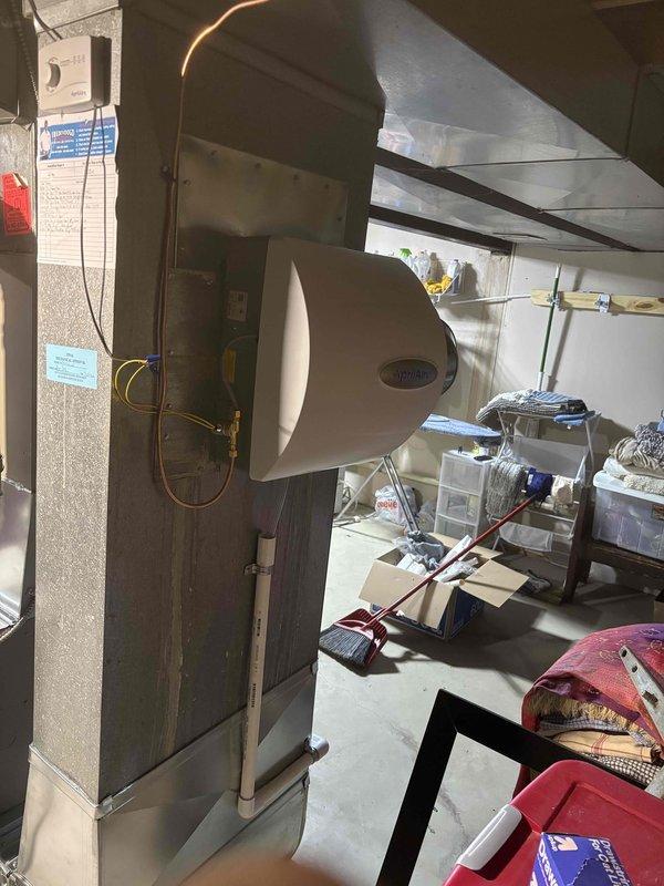 Completed full furnace installation in residential basement utility area. Installed new Carrier brand furnace unit on protective mat with proper positioning and clearances. Connected copper refrigerant lines and gas piping to furnace. Mounted white humidifier unit to side of furnace with appropriate tubing connections. Installed and configured galvanized steel ductwork with elbow configuration to direct airflow vertically and horizontally as required. Verified all manufacturer labels and safety stickers properly displayed on unit. Ensured proper venting and air handler integration. System tested and operational upon completion.