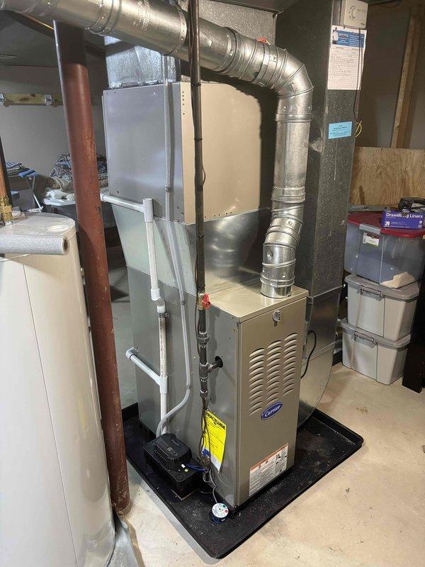 Completed full furnace installation in residential basement utility area. Installed new Carrier brand furnace unit on protective mat with proper positioning and clearances. Connected copper refrigerant lines and gas piping to furnace. Mounted white humidifier unit to side of furnace with appropriate tubing connections. Installed and configured galvanized steel ductwork with elbow configuration to direct airflow vertically and horizontally as required. Verified all manufacturer labels and safety stickers properly displayed on unit. Ensured proper venting and air handler integration. System tested and operational upon completion.