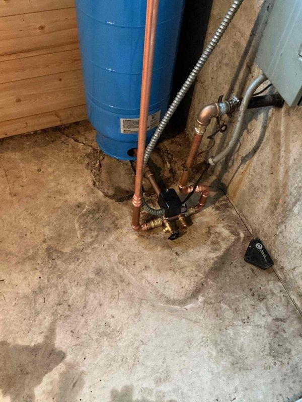 Completed well tank replacement in residential basement utility area. Removed existing failed pressure tank and installed new blue cylindrical well pressure tank with proper copper piping connections, pressure gauge assembly, brass fittings, and flexible stainless steel connector line to existing plumbing system. Verified all connections for proper operation and system pressurization.
