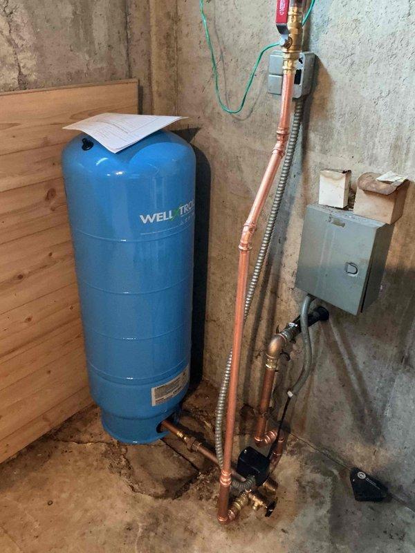 Completed well tank replacement in residential basement utility area. Removed existing failed pressure tank and installed new blue cylindrical well pressure tank with proper copper piping connections, pressure gauge assembly, brass fittings, and flexible stainless steel connector line to existing plumbing system. Verified all connections for proper operation and system pressurization.