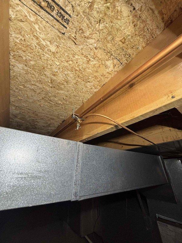 Responded to service call for humidifier with broken cover/lid that was no longer operational. Upon arrival, accessed basement mechanical systems and inspected humidifier installation mounted to ductwork. Unit age and manufacturer were unknown, possibly original to home construction. Documented existing installation configuration with copper water supply line secured to floor joists and humidifier mounted to HVAC ductwork. Assessed damage to cover assembly and provided recommendations for repair or replacement options to restore unit to working condition.