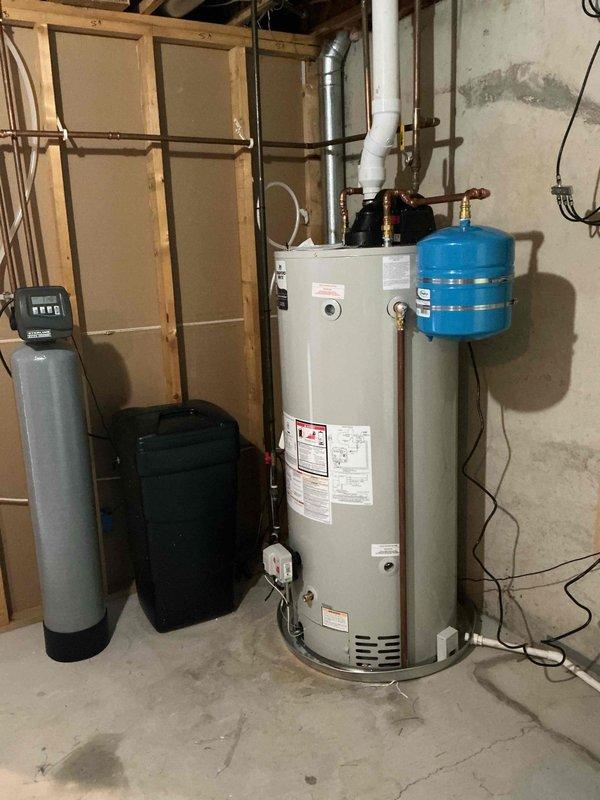 Completed installation of 75-gallon natural gas power vent water heater in basement utility area. Unit was positioned adjacent to existing water softener system, with proper venting installed through metal ductwork, blue expansion tank mounted to supply piping, and all connections made per manufacturer specifications using copper and PVC piping with appropriate gas valve assembly and electrical hookup.