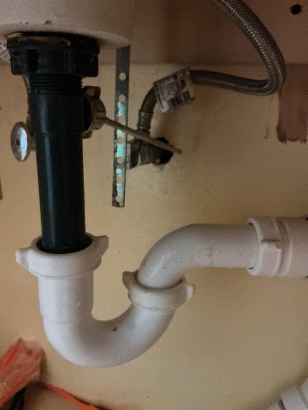 Responded to service call for kitchen sink valve with no resistance. Upon inspection, examined the shut-off valve assembly under the sink and assessed the plumbing configuration including the P-trap, tailpiece assembly, and water supply lines. Documented existing conditions with photographs showing the white PVC P-trap, black plastic drain tailpiece with adjustment mechanism, braided metal supply line, and mounting hardware. Verified the valve operation and inspected surrounding plumbing components for proper function and potential leak sources.